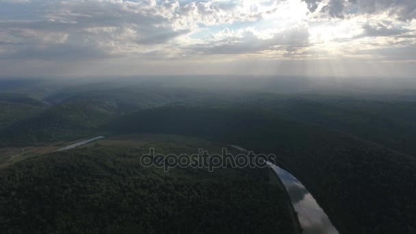 Tiro aéreo de montanhas cobertas com floresta de coníferas com rio e raios de sol através das nuvens . — Vídeo de Stock