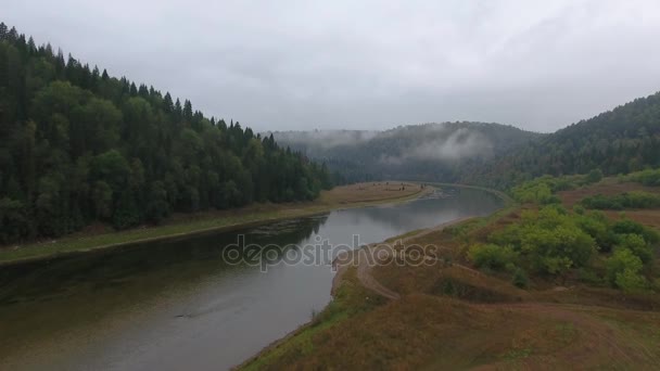 Légi repülő előre felvétel hegyi folyó erdővel borított hegyek között. Szürke esőfelhők. A folyó felett köd. — Stock videók