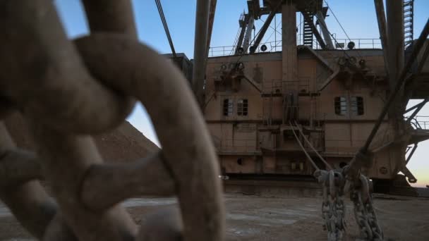 Tiro de mão de cadeia de balde maciça de escavadeira dragline de pé no lado da pedreira contra o pôr do sol no céu azul . — Vídeo de Stock