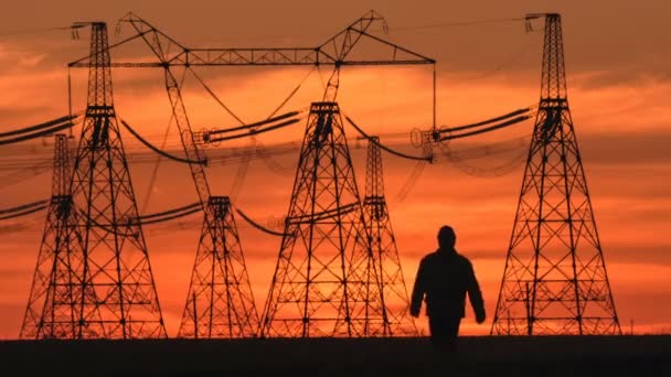 Wide shot van toezichthouder silhouet in harde hoed gaat langs de elektrische leidingen bij Rode zonsondergang tijdens een energie onderstation inspectie. — Stockvideo
