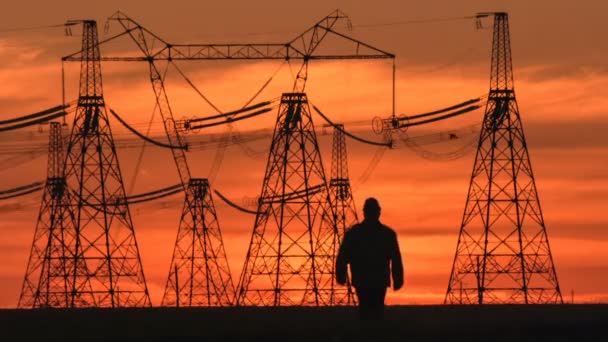 Wide shot van toezichthouder silhouet in harde hoed gaat langs de elektrische leidingen bij Rode zonsondergang tijdens een energie onderstation inspectie. — Stockvideo