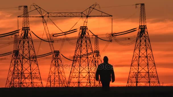 Wide shot van toezichthouder silhouet in harde hoed gaat langs de elektrische leidingen bij Rode zonsondergang tijdens een energie onderstation inspectie. — Stockvideo