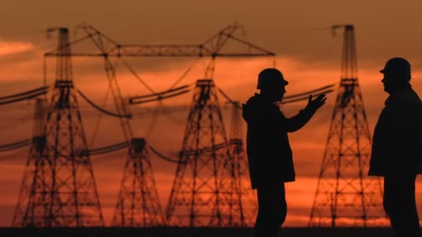 Amplia toma de dos ingenieros con sombrero duro discutiendo vigorosamente algo al atardecer rojo durante una inspección de la subestación de energía . — Vídeos de Stock