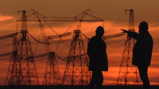 Bred sköt två ingenjörer i hård hatt kraftigt diskutera något i röda solnedgången under en energi transformatorstation inspektion. — Stockvideo