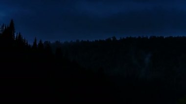 Dağ orman tarafından şafakta yüzen zaman atlamalı gri bulutlar altında geniş çekim.