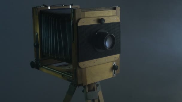 Kamerafahrt in der Mitte der Aufnahme einer alten hölzernen Fotokamera, die durch Sonnenlicht durch die Jalousien im grauen Hintergrund beleuchtet wird. — Stockvideo