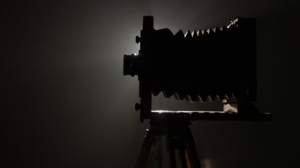 半ばショット ショットの古いビンテージ木製写真カメラのシルエットのゆっくり回転、黒い背景で光に対して. — ストック動画