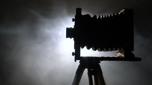 Mid-Shot-Aufnahme einer alten hölzernen Fotokamera-Silhouette, die sich langsam gegen das Licht im schwarzen Hintergrund dreht. — Stockvideo