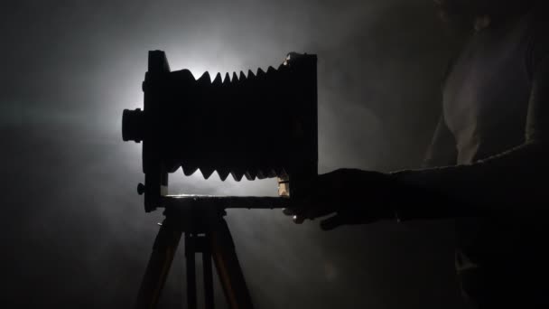 중간 샷 수염된 사진 작가의 오래 된 빈티지 나무 사진 카메라와 검은 배경에서 빛에 대 한 촬영 사진을 조정. — 비디오