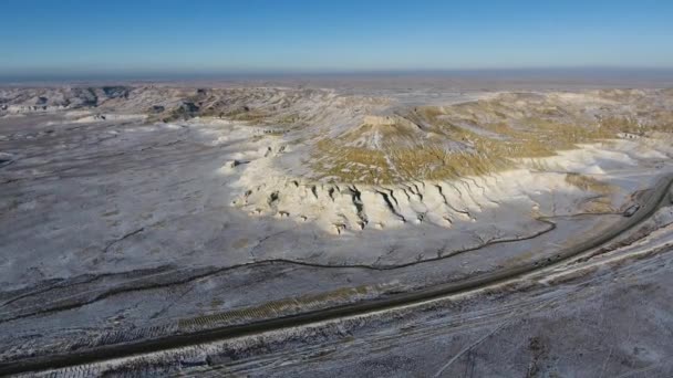 Luchtfoto van drie SUV's verplaatsen langs de snelweg in de sneeuw-coversd zandstrand bergen in de winter. West Kazachstan, Mangyshlak schiereiland. — Stockvideo