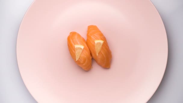 Vue de dessus de la filature de deux sushis de saumon avec des tranches de citron sur la plaque rose filante . — Video