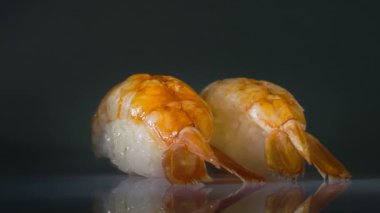 İki karides nigiri sushi siyah arkaplanda dönüyor.