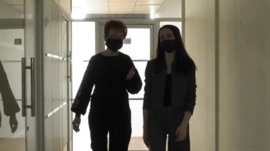 Salgın bir COVID-19 sırasında ofis işi. Genç bir iş kadını ve koruyucu maskeli yaşlı bir kadın ofis koridorunda konuşuyorlar..