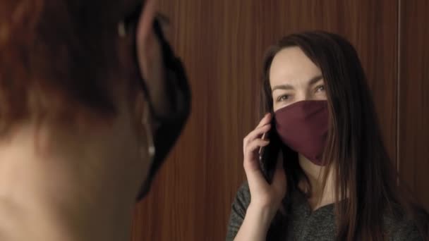 Office work during a pandemic COVID-19. Young business woman talking on smartphone and an elderly woman in protective masks are talking in office coridor. — Stock Video