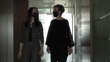 Salgın bir COVID-19 sırasında ofis işi. Genç bir iş kadını ve koruyucu maskeli yaşlı bir kadın ofis koridorunda konuşuyorlar..