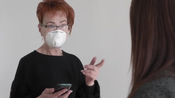 Büroarbeit während einer Pandemie COVID-19. Junge Geschäftsfrau und eine ältere Frau, die mit Schutzmasken auf dem Smartphone spricht, unterhalten sich im Büro. — Stockvideo