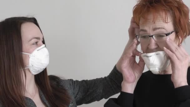 Jovem mulher em máscara protetora ajuda a colocar uma máscara para uma mulher idosa . — Vídeo de Stock