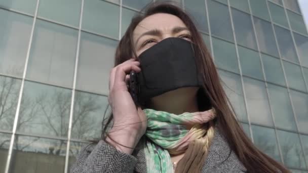 Portrét ustaraně ženy stojící na ulici v ochranné masce a používající smartphone. Mladá zaměstnaná dívka čte zprávy o koronaviru. Covid-19, pandemie, nebezpečí. — Stock video