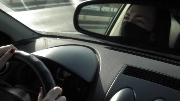 Reflectie van een vrouw met een gezichtsmasker Covid-19 in een achteruitkijkspiegel van een auto tijdens het rijden in een file in de avond tijdens coronavirus — Stockvideo