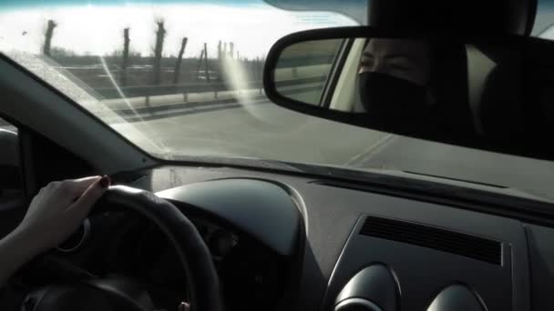 Egy nő arcmaszkot visel Covid-19 egy visszapillantó tükörben egy autó vezetés közben egy dugóban este a koronavírus alatt — Stock videók