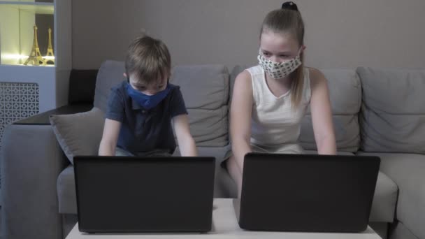 在COVID 19大流行期间，以戴防护面具的可爱男孩和女孩为研究对象，在网上用电脑打字，准备考试. — 图库视频影像
