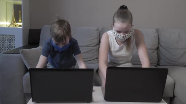 Focalizzato carino ragazzo e ragazza in maschera protettiva utilizzando laptop ricerca informazioni corso internet studio online in app digitando sul computer prepararsi per l'esame di prova sedersi sul divano di casa durante la pandemia COVID 19 . — Video Stock