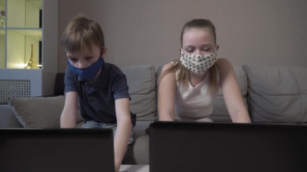 Focalizzato carino ragazzo e ragazza in maschera protettiva utilizzando laptop ricerca informazioni corso internet studio online in app digitando sul computer prepararsi per l'esame di prova sedersi sul divano di casa durante la pandemia COVID 19 . — Video Stock