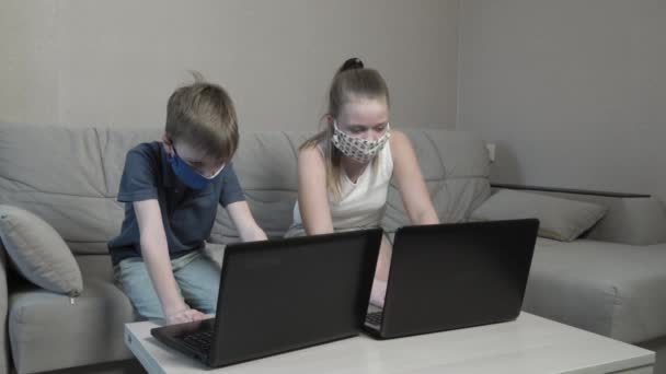 Εστιασμένη χαριτωμένο αγόρι και κορίτσι σε προστατευτική μάσκα χρησιμοποιώντας πληροφορίες αναζήτησης laptop internet μελέτη μαθημάτων σε απευθείας σύνδεση στην πληκτρολόγηση app στον υπολογιστή προετοιμασία για τις εξετάσεις δοκιμή καθίσει στο σπίτι καναπέ κατά τη διάρκεια της πανδημίας COVID 19. — Αρχείο Βίντεο