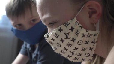 Odaklanmış, koruyucu maskeli tatlı bir çocuk ve kız. İnternette dizüstü bilgisayarda internet kursu çalışması, test sınavına hazırlık, COVID 19 salgını sırasında kanepede otur..