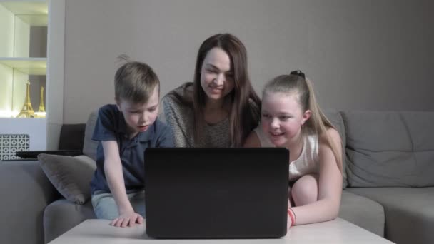 フォーカス可愛いです男の子と女の子と彼らのお母さん使用してノートパソコンの勉強オンラインでアプリタイピング上のコンピュータ試験で自宅ソファに座っている間にザCOVID 19パンデミック. — ストック動画