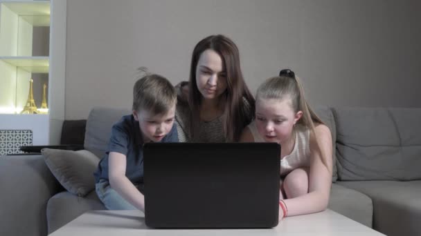 Орієнтований милий хлопчик і дівчинка з мамою, використовуючи ноутбук в онлайн-додатку, вводячи на комп'ютерний іспит, сидять на домашньому дивані під час пандемії COVID 19 . — стокове відео