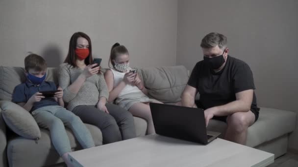 Семья в защитных масках, перчатки с помощью гаджетов дома в изоляции от пандемии коронавируса. Мама, папа, сын смотрят фильм вместе за компьютером. Глобальная эпидемия COVID-19. — стоковое видео