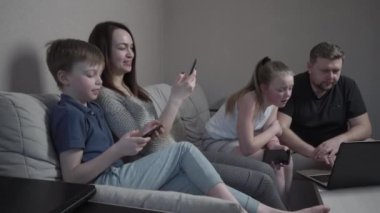 Aile eldivenleri evde koronavirüs salgını karantinasında cihazlar kullanıyor. Anne, baba, oğul ve kız bilgisayarda film izliyorlar. Dünya çapında küresel COVID-19 salgını.