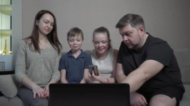 Aile eldivenleri evde koronavirüs salgını karantinasında cihazlar kullanıyor. Anne, baba, oğul ve kız bilgisayarda film izliyorlar. Dünya çapında küresel COVID-19 salgını.