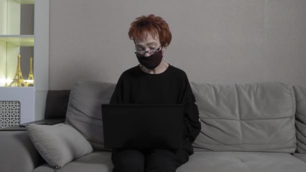 戴防护面具的老年妇女在电脑上通过Skype与家人交流。全球COVID-19流行病. — 图库视频影像
