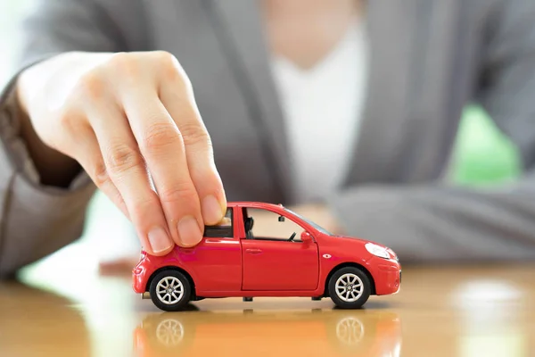 Mujer de negocios junto a un escritorio sosteniendo un coche de juguete . —  Fotos de Stock