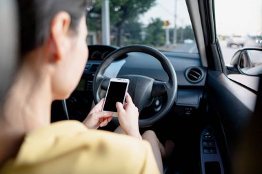 Arabada genç bir kadın araba kullanırken akıllı telefonunu kontrol ediyor.