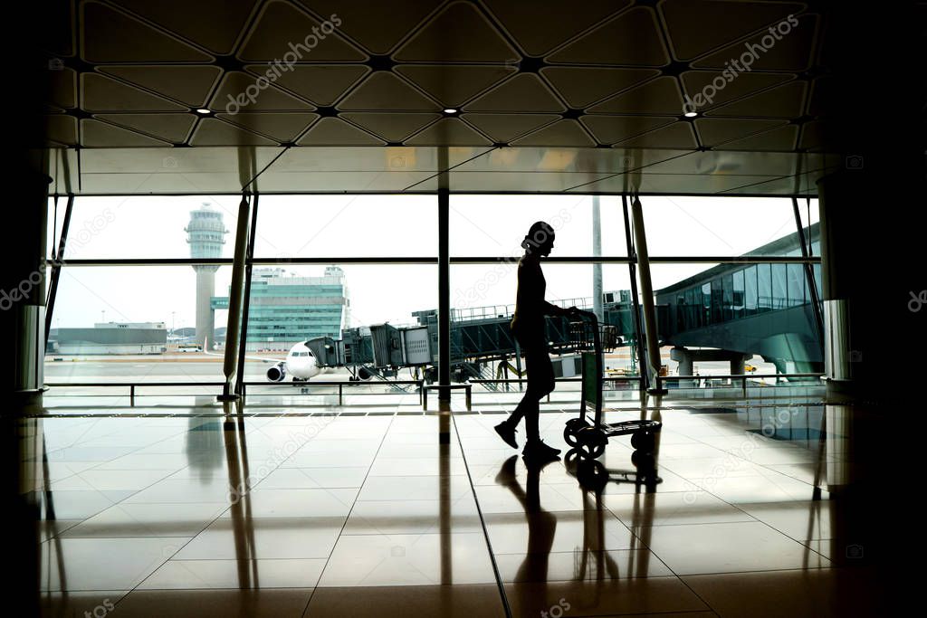 Silhouette of woman with walking to board flight in airport terminal. Passenger at airport terminal with luggage car