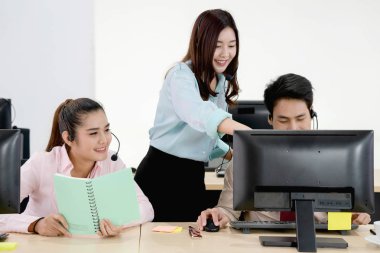 Kulaklık takan çağrı merkezi çalışanları bilgisayar kullanıyor. Kadın yeni iş arkadaşına pazarlama veritabanı programını anlatıyor. Paylaşılan masada oturan meşgul servis operatörleri, yardım ekibi toplantılarını anlatıyor.