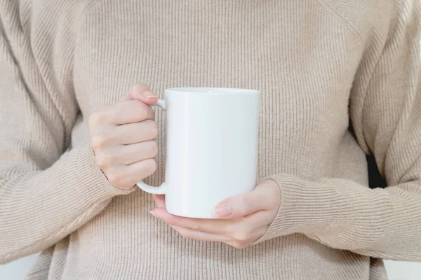 Sıcak kazaklı kadın elinde beyaz kupa tutuyor.