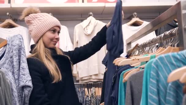 Mujer joven elige la ropa en la tienda — Vídeo de stock