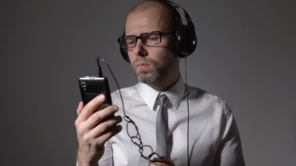 Zakenman in een shirt en grote koptelefoon, luisteren naar trendy nummer vanaf uw apparaat. — Stockvideo