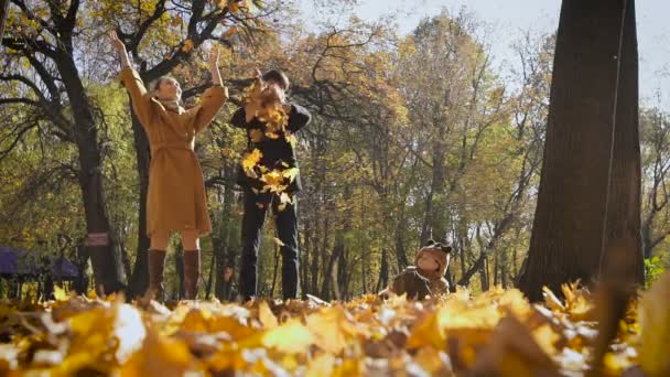 Šťastná rodina hraje s podzimní listy v parku. Máma a táta zvracet Lea, ve vzduchu. Malé dítě pohled na ně a baví.