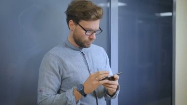 İş yerinde bir koridorda duvara yaslanmış haliyle işadamı cep telefonunu denetler
