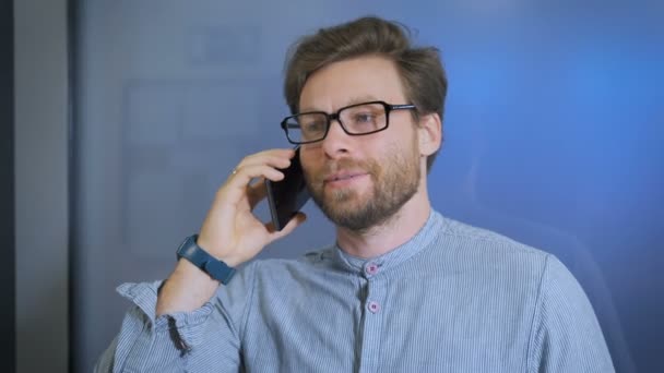 Ung man talar i mobiltelefon på moderna kontor — Stockvideo
