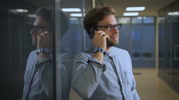 Hombre rubio en un centro de negocios hablando en su teléfono inteligente negro . — Vídeo de stock