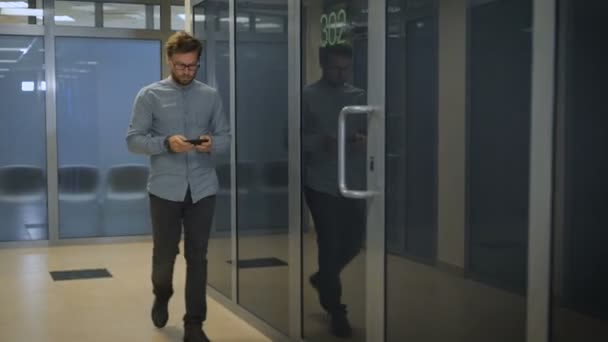 Joven emprendedor camina en corredor con tablet teléfono inteligente — Vídeos de Stock