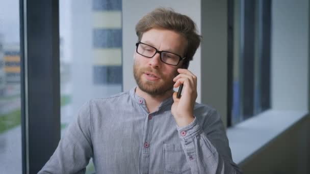 Blond man står vid fönstret och pratar i telefon. — Stockvideo