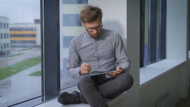 Молодий претендент на роботу сидить у вікні і використовує планшет — стокове відео