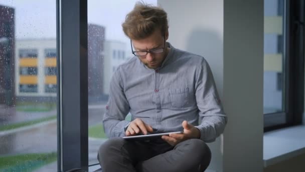 Estudiante universitario en el pasillo sentado en el alféizar de la ventana y viendo noticias en la tableta — Vídeo de stock